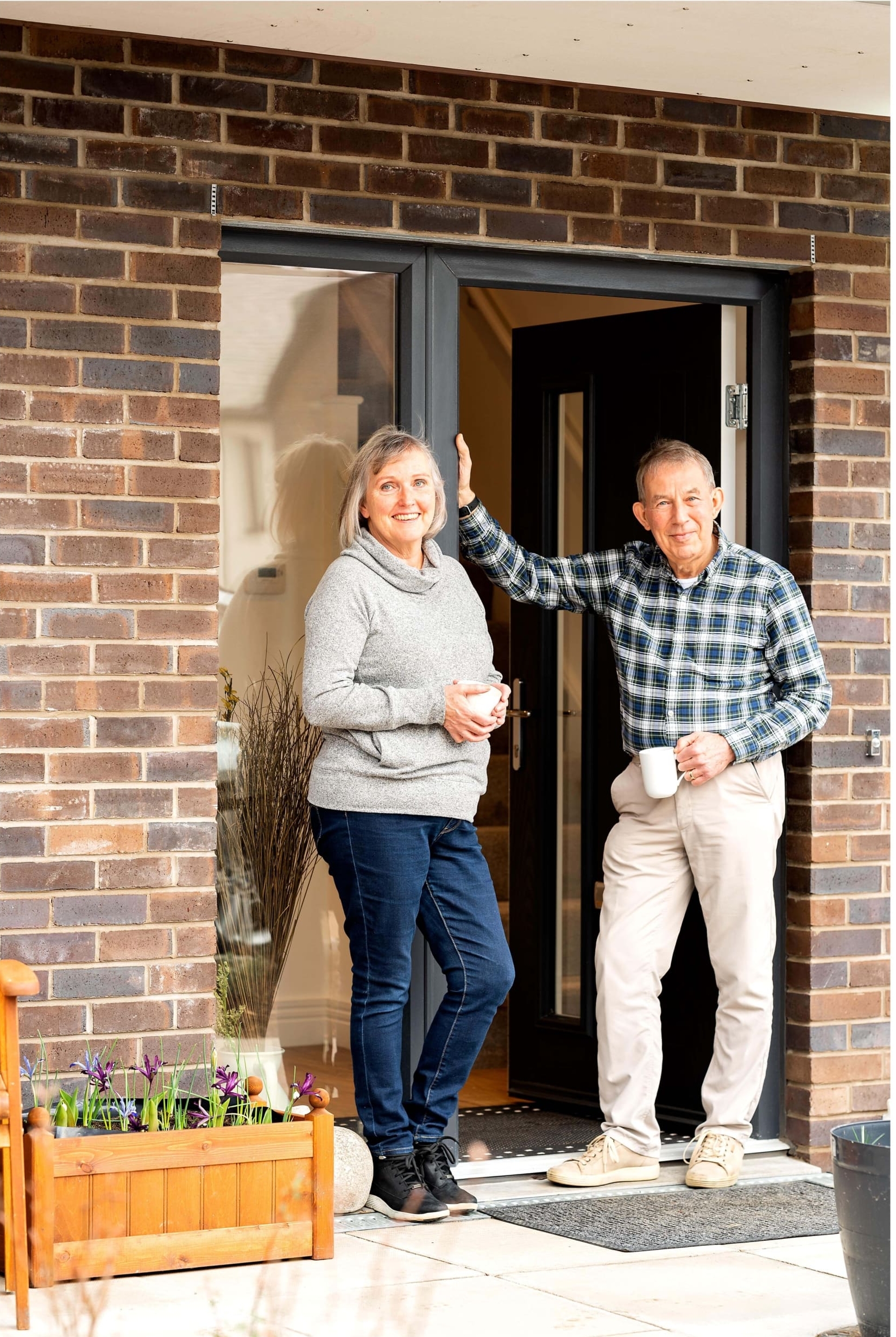 Couple stood in doorway of their new build home in the Scottish Borders. Both holding mugs in front of open doorway with brick facade surrounding doorframe