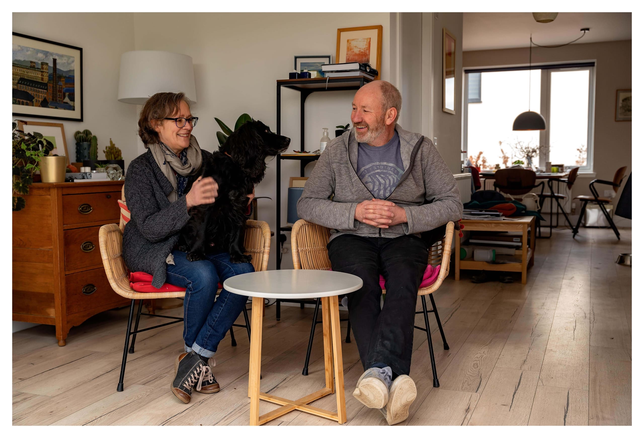 Couple sitting on armchairs in their new build home with open-plan living area. Woman has black dog on her lap