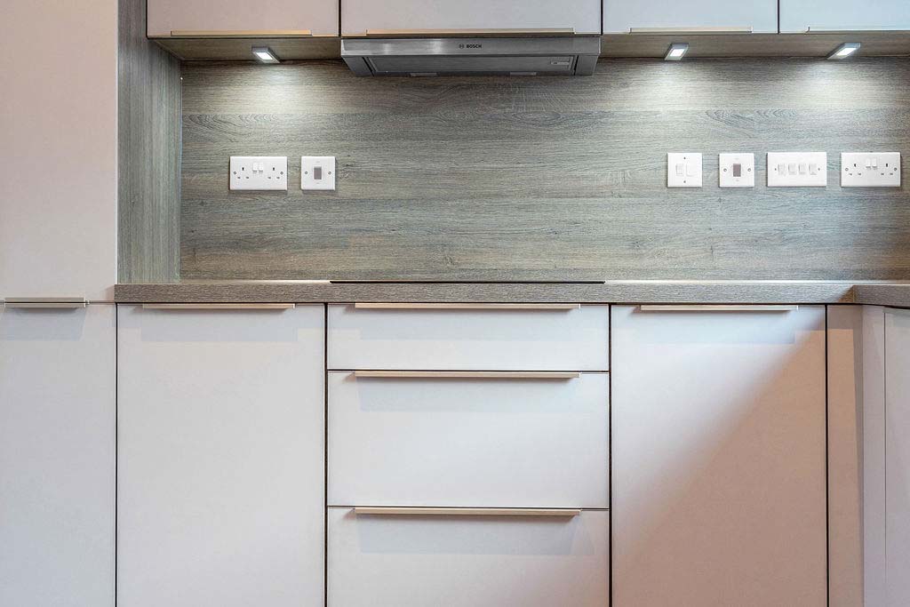 Light coloured kitchen with metal handles and a dark grey wall panelling in a new home, the borders