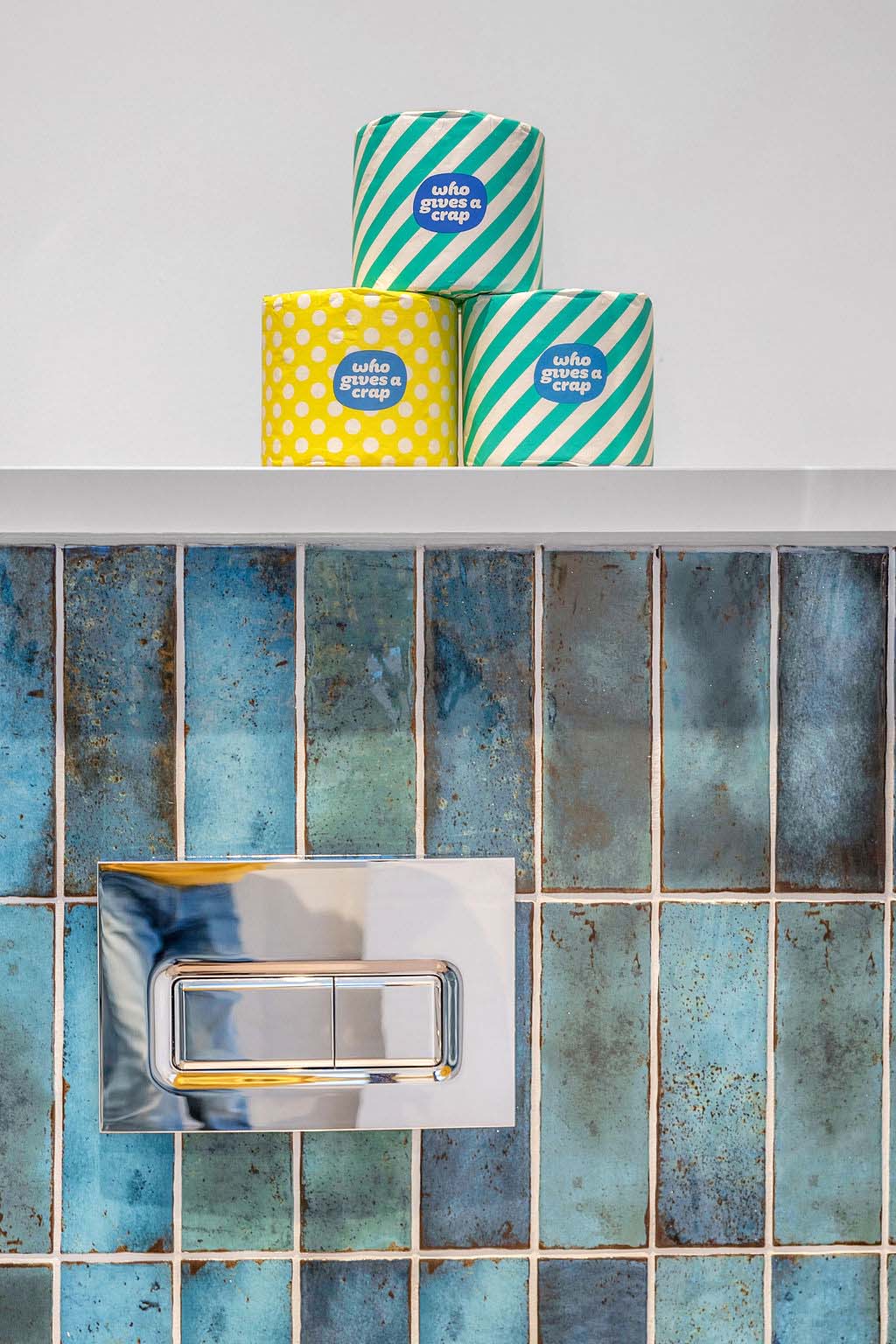 Tiled bathroom flushplate with colourful toilet rolls to shelf in the new homes for sale in Peebles