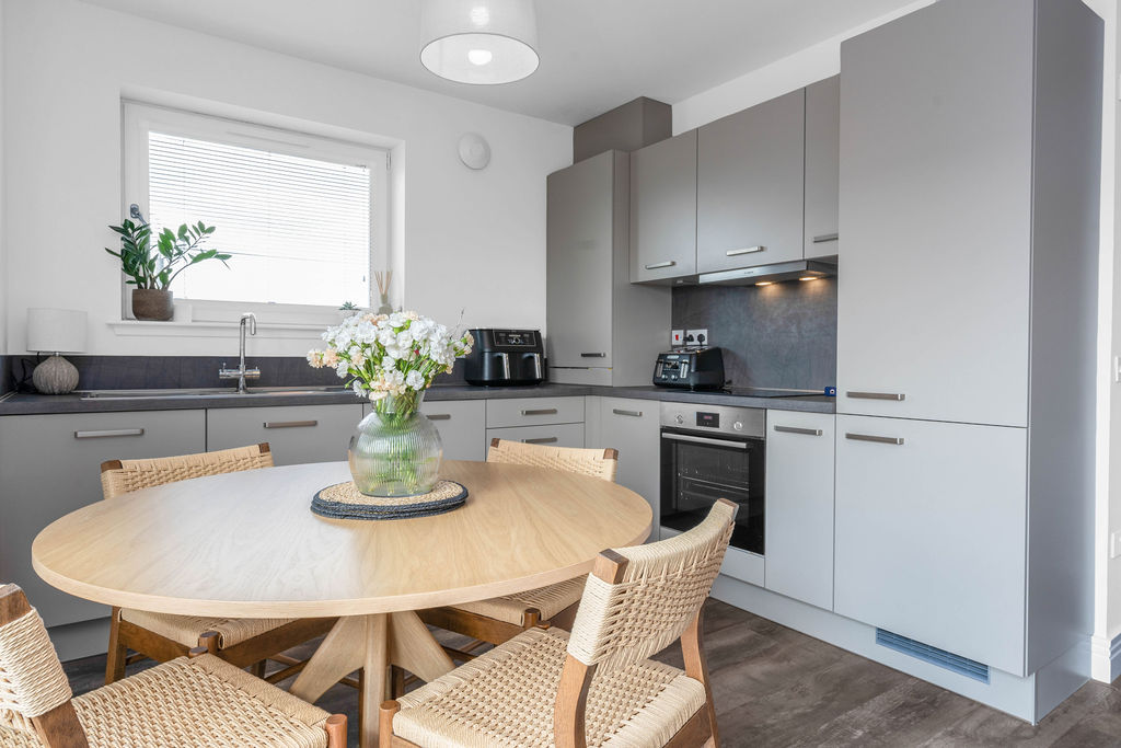 Modern grey kitchen with integrated Bosch appliances with a dining table and chairs in foreground of a new home apartment, Fife