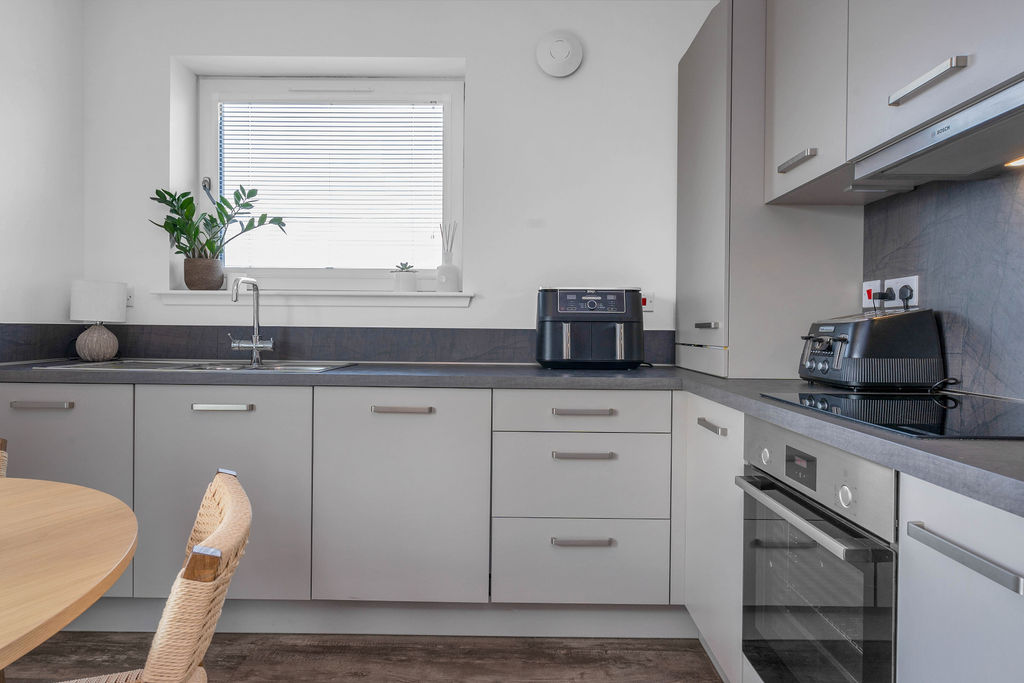 Modern grey kitchen with integrated Bosch appliances with a dining table and chairs in foreground of a new home apartment, Fife