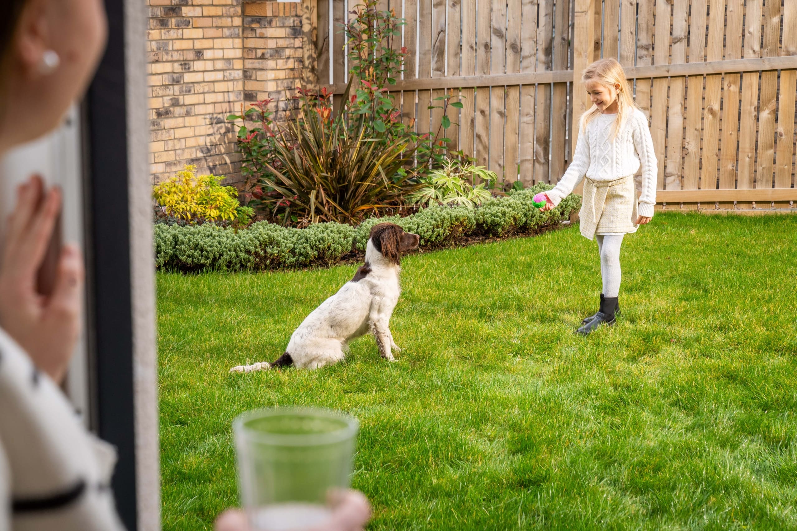 Girl in garden with dog, whilst female looks out from patio doors from a new home in the Borders