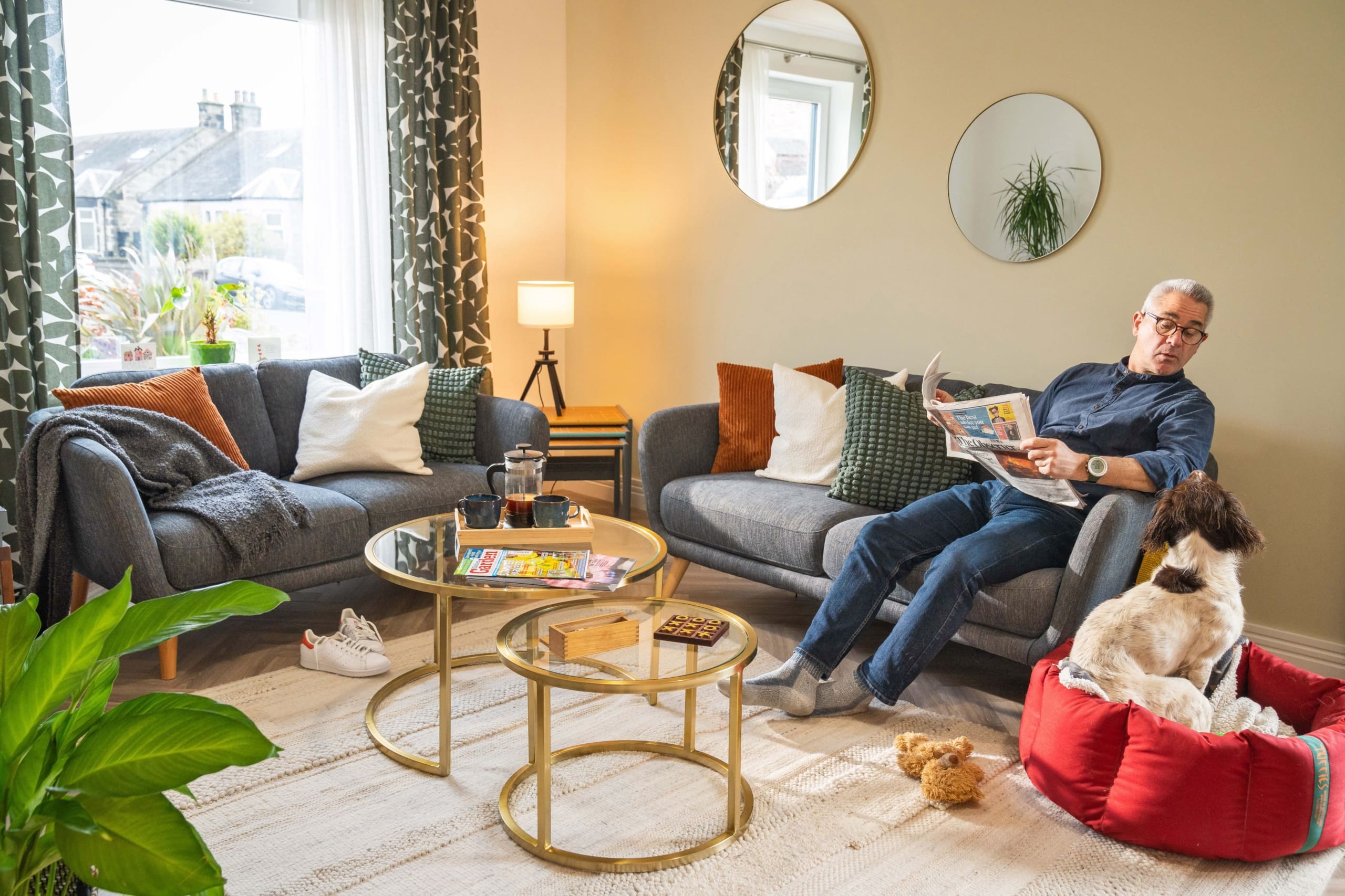 Man in livingroom on a grey sofa with colourful throw cushions, looking at a dog in a new build home in Peebles