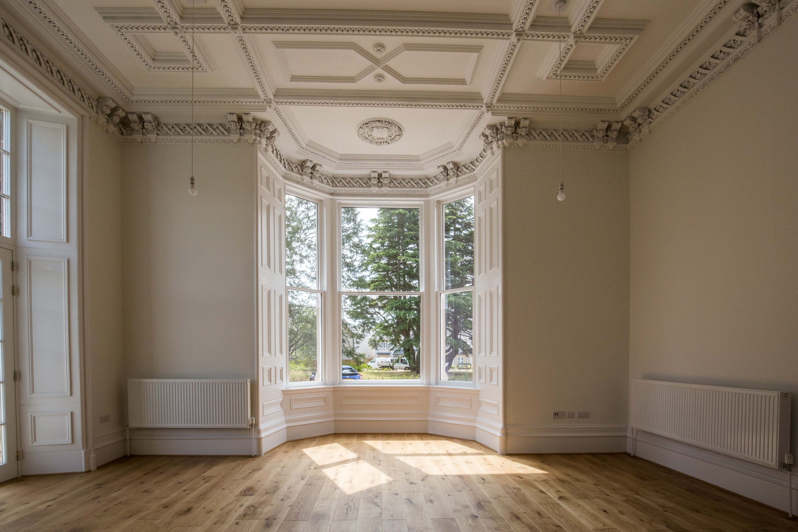 Large room in refurbished Ashludie House. Bay windows and cornicing feature with wooden floors and white walls.