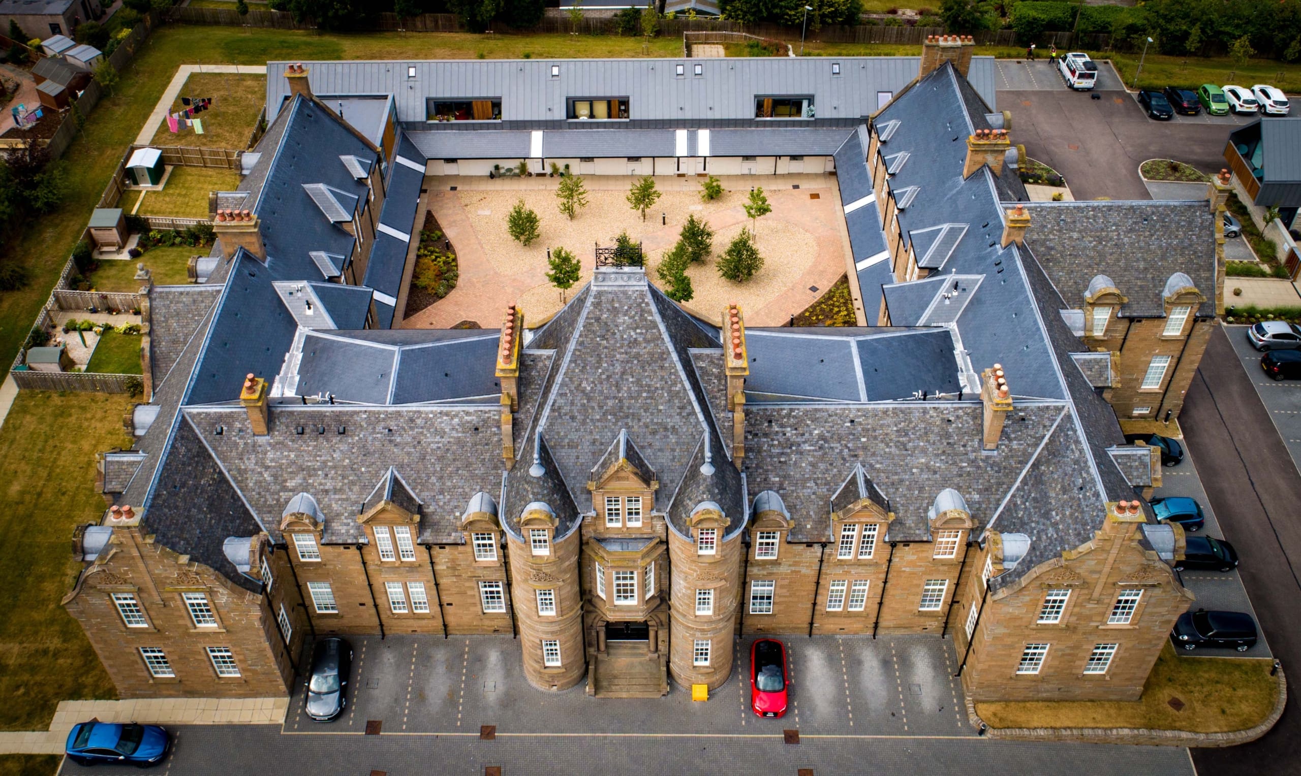 Ariel view over building with courtyard to centre with landscaping. Car parking to front of building of new build homes in renovated building in Dundee