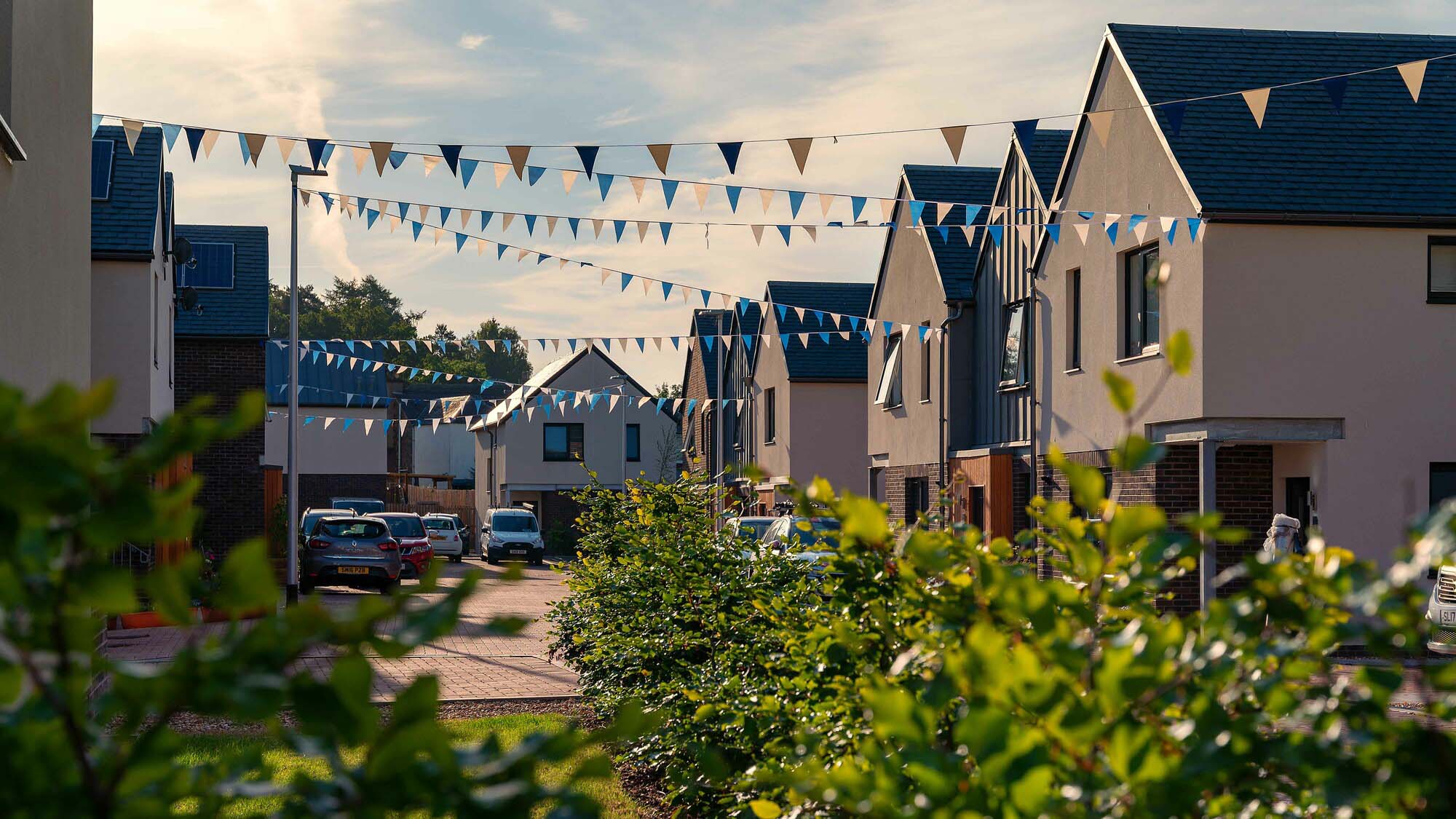 View down street of new build homes in Innerleithen, Scottish Borders. Bunting hanging between homes with green bushes in foreground
