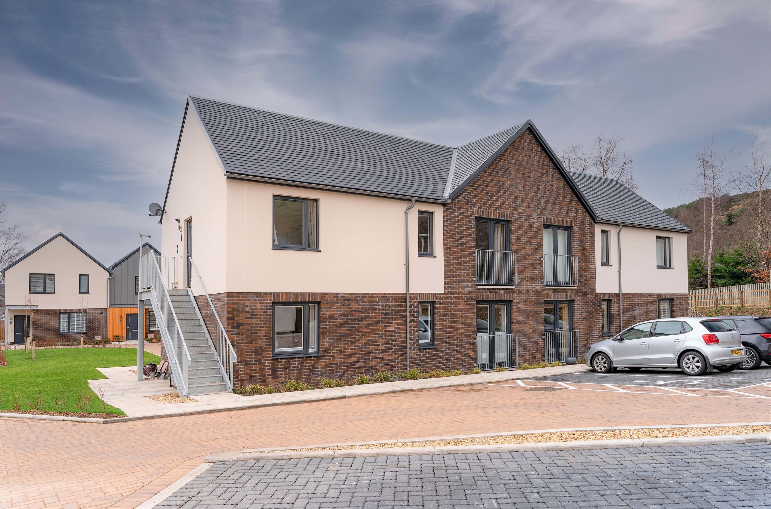 External of a new build apartment block at Caerlee Mill, Innerleithen in the Scottish Borders. Parking with cars to front of building.