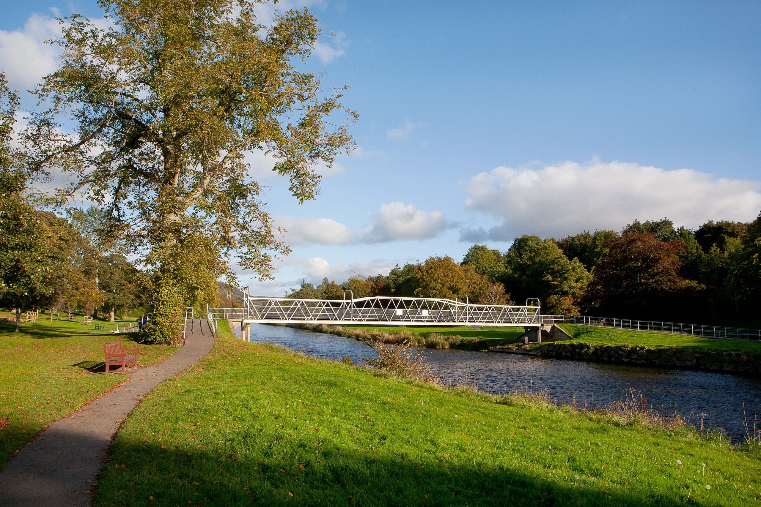 Views of grassy riverbank with river, footbridge and trees, in Peebles, The Borders