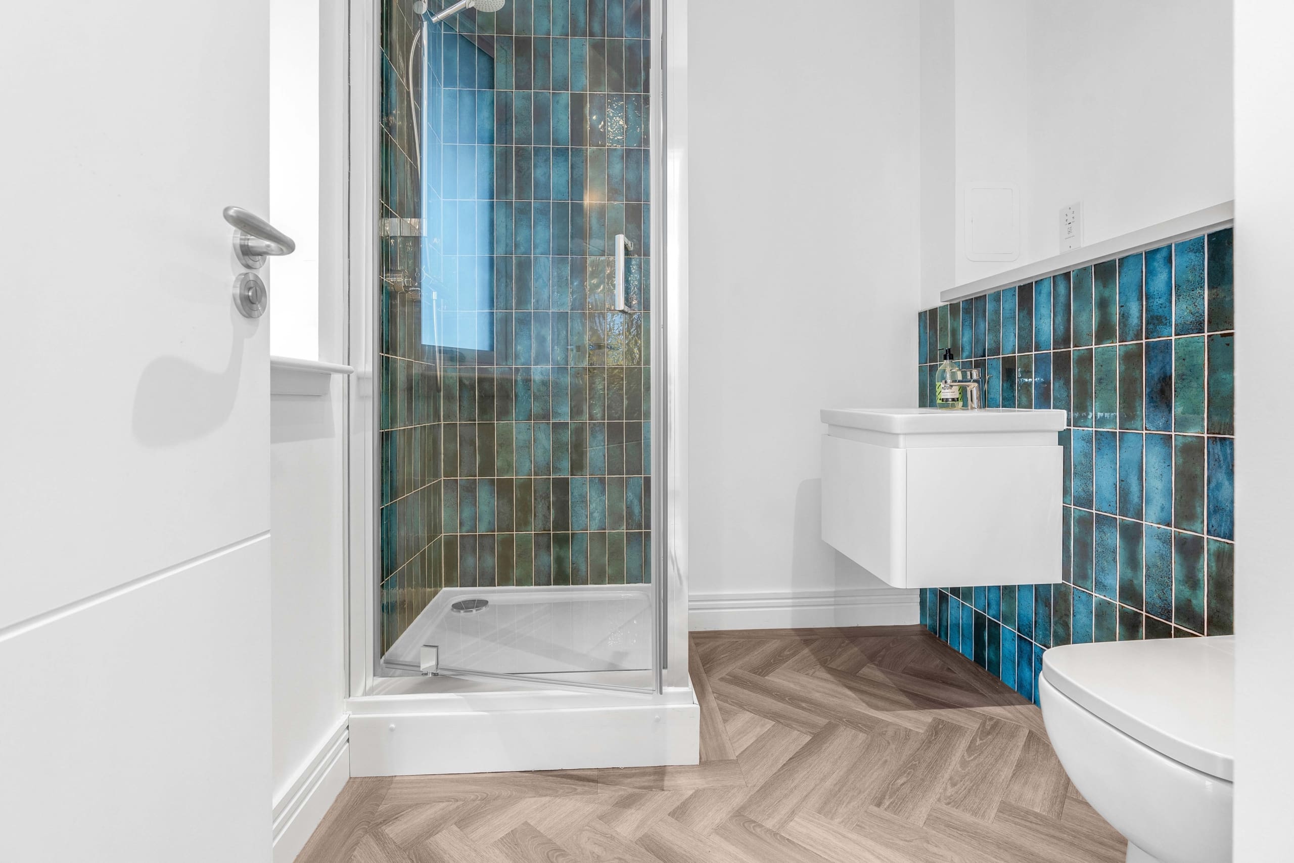 Downstairs shower room with white sanitaryware, chrome fittings and turquoise tiling to back of sink and shower at Allanbank, Lauder