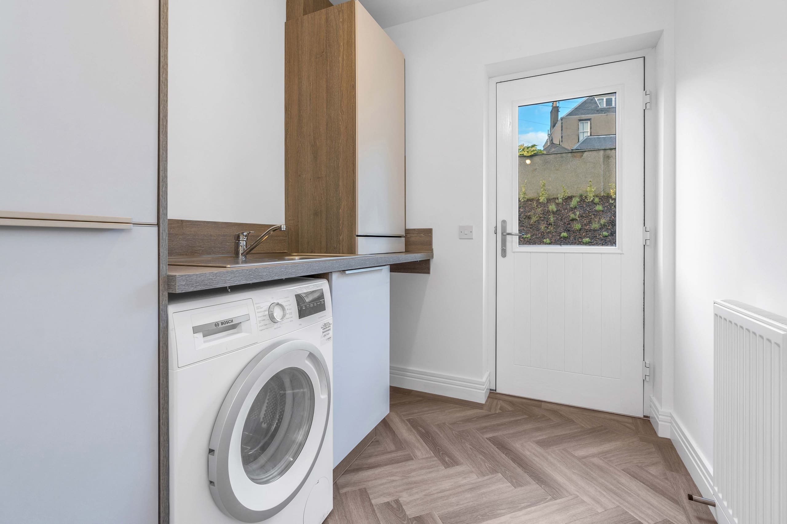 Utility room with white cupboards and built in washing machine and back door into garden in a 4 bedroom new build home in Lauder