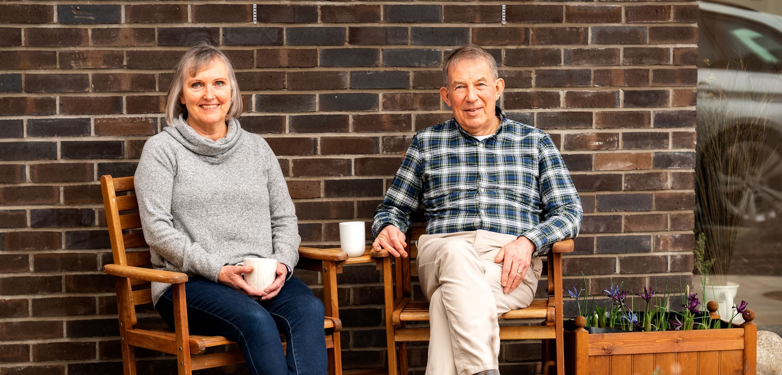 Couple sat on wooden chairs outside their new build home in Innerleithen